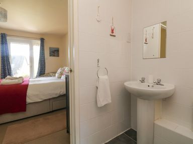 A bathroom with a pedestal sink and towel ring next to a bedroom with a bed and window at Valley Lodge 44 in Callington