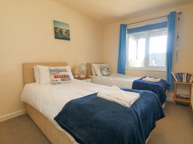 A bedroom with two single beds with blue blankets and pillows and a window with blue curtains at Valley Lodge 44 in Callington