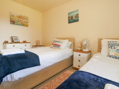 A bedroom with two single beds pillows and blankets bedside tables a chest of drawers and wall art at Valley Lodge 44 in Callington