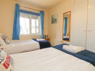 A bedroom with two single beds blue curtains a wall mirror and a small wooden table at Valley Lodge 44 in Callington