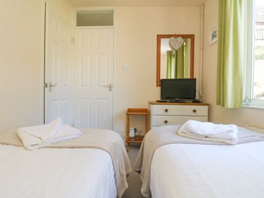 A bedroom with two single beds a chest of drawers with a television a mirror and green curtains at Valley Lodge 44 in Callington