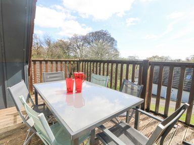 An outdoor balcony with a glass table and six chairs with red pitcher and glasses on the table at Valley Lodge 44 in Callington