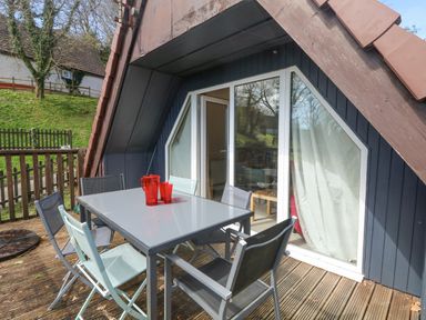 An outdoor patio with a rectangular table and six chairs near a triangular window and door at Valley Lodge 44 in Callington