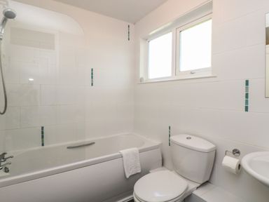 A bathroom with a bathtub shower, toilet, sink, and window at Valley Lodge 58 Callington