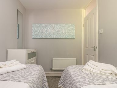 A bedroom with two beds white chest of drawers a wall radiator and a door at Valley Lodge 58 in Callington