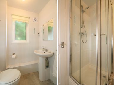 A bathroom with a toilet, sink, mirror, window, and a separate shower with glass doors at Valley Lodge 58 in Callington