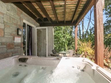 An outdoor patio with a hot tub table and chairs under a wooden roof surrounded by trees at Valley Lodge 58 in Callington