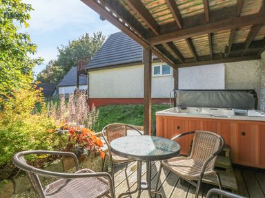 An outdoor covered patio with a hot tub a round glass table and wicker chairs at Valley Lodge 58 in Callington