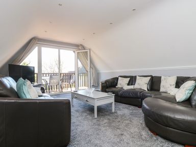 A living room with black leather sofas white coffee table and sliding glass doors leading to a balcony at Valley Lodge 58 in Callington