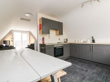 A kitchen with grey cabinets a white table and a living area with sofas and a television at Valley Lodge 58 in Callington