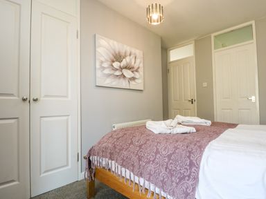 A bedroom with a bed covered with a patterned blanket and two folded towels on top a flower painting on the wall and two doors at Valley Lodge 58 in Callington