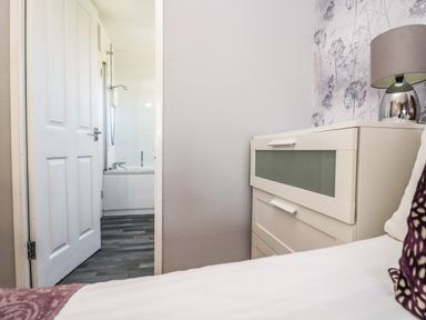 A bedroom with a bedside table with a lamp and an open door leading to a bathroom at Valley Lodge 58 in Callington