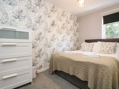 A bedroom with a bed with pillows and a blanket next to a white chest of drawers and a window at Valley Lodge 58 in Callington