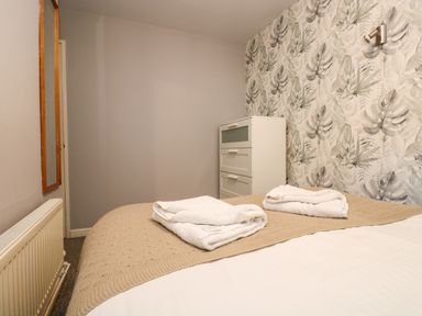 A bedroom with a bed covered by a beige blanket and two folded white towels on top a white chest of drawers and a wall mirror at Valley Lodge 58 in Callington