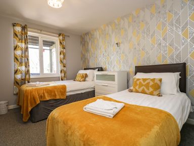 A bedroom with two single beds yellow blankets and pillows white chest of drawers and patterned wallpaper at Valley Lodge 58 in Callington