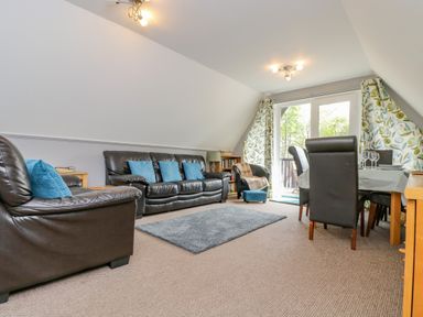 A living room with black leather sofas blue cushions a dining table and floral curtains at Valley Lodge 5 Callington
