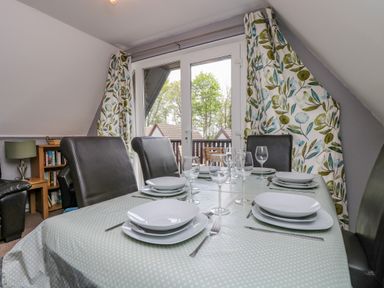 A dining room with a table set with plates and glasses near a window with floral curtains at Valley Lodge 5 in Callington