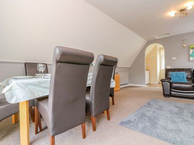 A dining area with dark chairs and a table set with glasses next to a living space with a dark sofa and blue cushion at Valley Lodge 5 in Callington