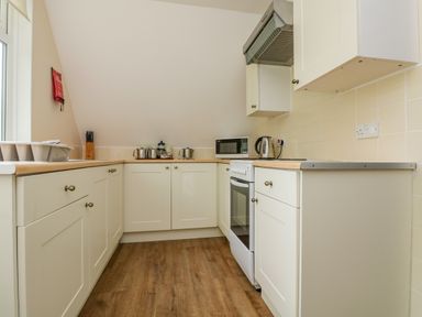 A kitchen with white cabinets a microwave kettle stove and wooden floor at Valley Lodge 5 in Callington