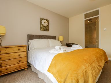 A bedroom with a double bed with white bedding and yellow blanket two bedside lamps and wooden chest of drawers at Valley Lodge 5 Callington