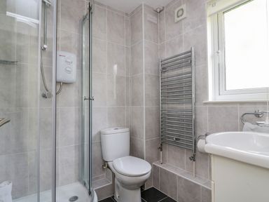 A bathroom with a shower, toilet, sink, towel radiator, and window at Valley Lodge 5 in Callington
