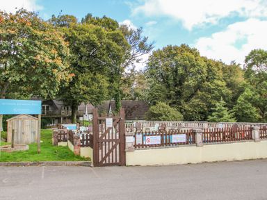 An outdoor swimming pool area with a wooden fence and gate surrounded by trees at Valley Lodge 5 in Callington