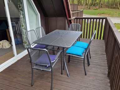 An outdoor wooden deck with a metal table and six metal chairs with blue and purple cushions at Valley Lodge 5 in Callington