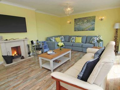 A living room with a beige sofa a blue corner sofa a wooden coffee table a fireplace and a wall-mounted TV at Windrush in Mawgan Porth