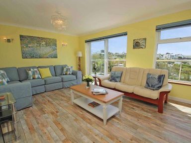 A living room with two sofas a wooden coffee table and large windows at Windrush in Mawgan Porth