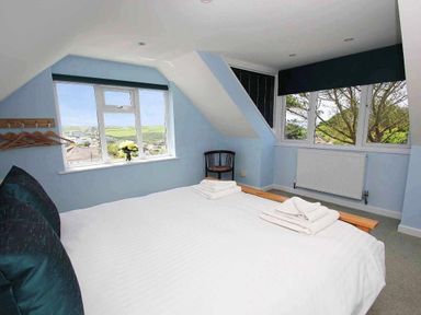 A bedroom with a bed a chair towels on the bed a window with a view and hangers on the wall at Windrush in Mawgan Porth