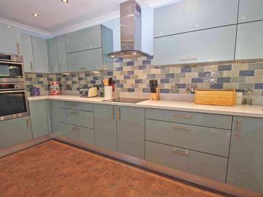 A kitchen with blue cabinets, tiled backsplash, built-in oven, countertop appliances, and cooking utensils at Windrush in Mawgan Porth