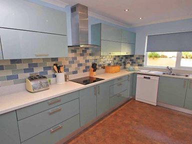 A kitchen with blue cabinets a tiled backsplash countertop appliances and a window at Windrush in Mawgan Porth