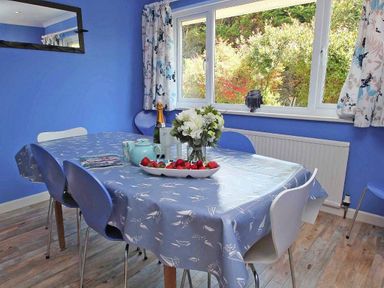 A dining room with a table set with strawberries flowers and a teapot at Windrush in Mawgan Porth