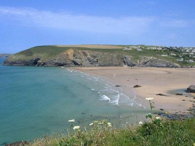 A coastal beach with waves and cliffs with houses on top at Windrush in Mawgan Porth