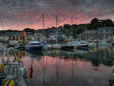 Boats docked at a harbor with buildings and a sunset sky at Windrush in Mawgan Porth