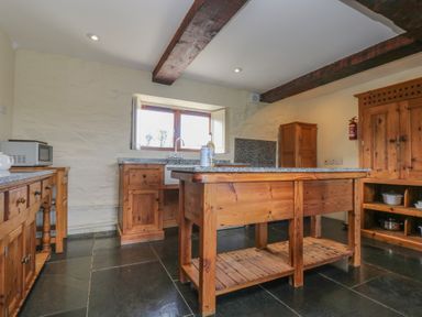 A kitchen with wooden cabinets a central wooden island a window above a sink and a microwave on a countertop at Marhayes in Camelford