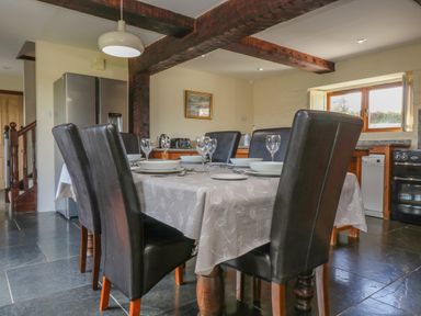 A dining area with a table set for six with plates and glasses in a kitchen with wooden beams at Marhayes Camelford