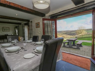 A dining area with a table set for six next to open doors showing an outdoor picnic table and countryside view at Marhayes in Camelford