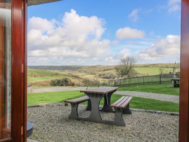 A picnic table with benches on a gravel patio overlooking grassy fields and hills at Marhayes in Camelford