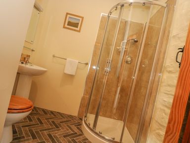 A bathroom with a curved glass shower enclosure a toilet with a wooden seat a pedestal sink and a towel hanging on a rail at Marhayes in Camelford
