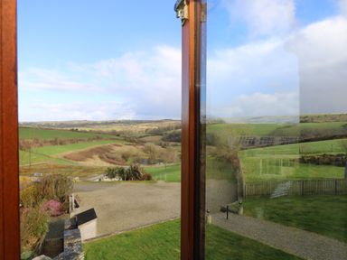 A rural landscape with grassy fields and hills viewed through a window at Marhayes in Camelford