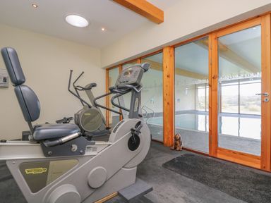 An exercise room with stationary bikes and a view of an indoor pool through glass doors at Marhayes in Camelford