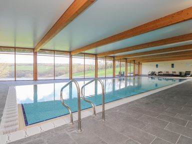 An indoor swimming pool with metal handrails large windows showing outside view and seating area at Marhayes in Camelford