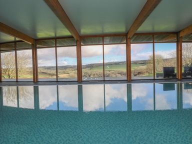 An indoor swimming pool with large windows showing a countryside view at Marhayes in Camelford