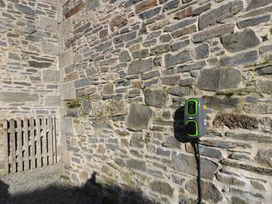 An outdoor stone wall with an electric vehicle charging station attached and a wooden fence on the left at Marhayes in Camelford