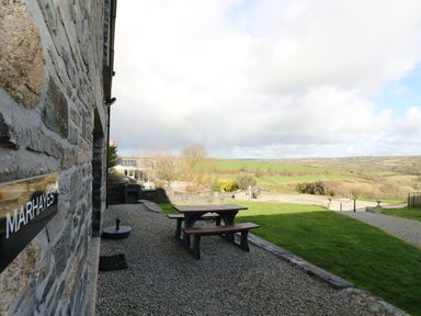 A stone building with a sign reading Marhayes a picnic bench on gravel and a grassy area with countryside views at Marhayes Camelford