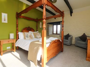 A bedroom with a four poster wooden bed pillows bedside table with lamp two armchairs and window at Marhayes Camelford