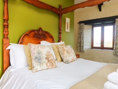 A bedroom with a wooden four-poster bed with patterned pillows and a window with floral curtains at Marhayes Camelford