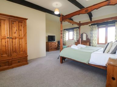 A bedroom with a wooden four poster bed dresser wardrobe and windows at Marhayes in Camelford