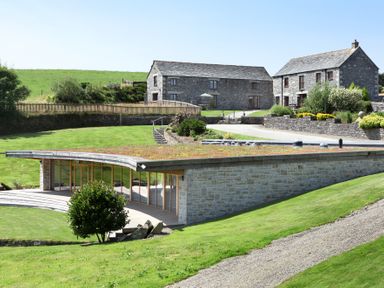 A stone modern building with grass roof near two traditional stone houses on a grassy landscape at Westhayes in Camelford
